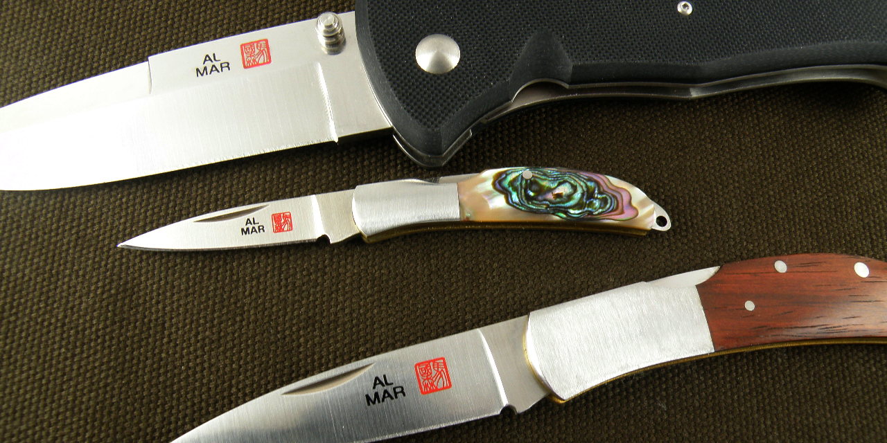 three al mar blades on a dark surface, open, showing the bright steel blades and gorgeous fit and finish