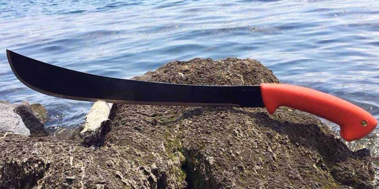 Sturdy machete, with a blaze orange/high visibility handle shown on a rock with slightly choppy water in the background.
